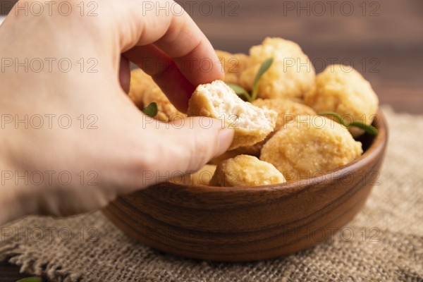 Fried crispy Chicken Nuggets with ketchup, microgreen on brown wooden background and linen textile with hand. side view, close up, selective focus