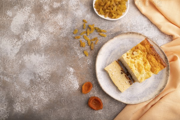 ?ottage cheese ?asserole, Curd cake, with dried apricots and raisins on brown concrete background and orange textile, top view, flat lay, copy space, minimalism