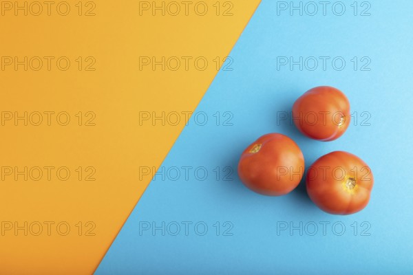 Red tomato on blue and orange pastel paper background. Top view, flat lay, copy space. healthy food, vegetable, minimalism