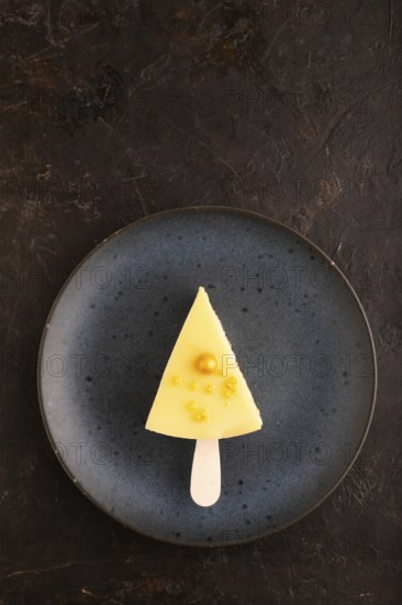 Yellow Cake pop with sprinkles on blue ceramic plate on black concrete background, top view, flat lay, copy space, minimalism