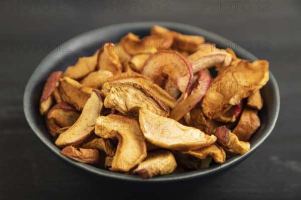 Dried Apples in ceramic bowl on black wooden background. Side view, close up. healthy food, minimalism. sweet, selective focus