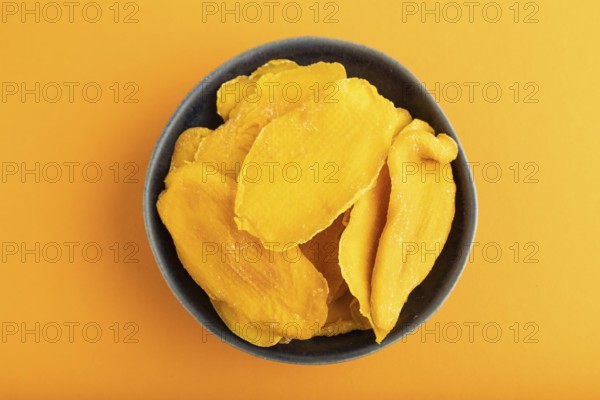 Dried Mango in blue ceramic bowl on orange pastel paper background. Top view, copy space, flat lay. healthy food, minimalism