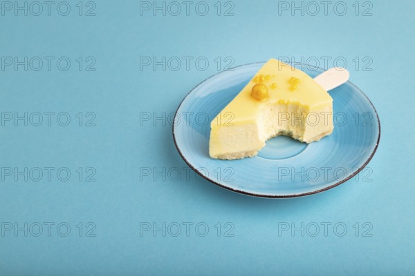 Bitten Yellow Cake pop with sprinkles on blue ceramic plate on blue pastel paper background, side view, copy space, minimalism