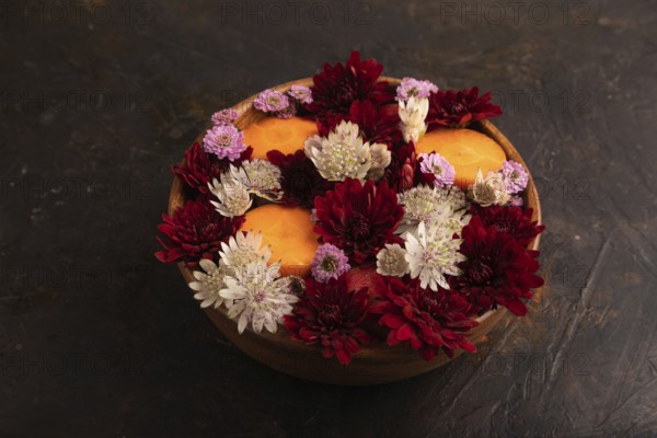Wooden bowl with carrot slices and red Chrysanthemum flowers, Astrantia flowers, flower salad on black concrete background, side view, close up, minimalism
