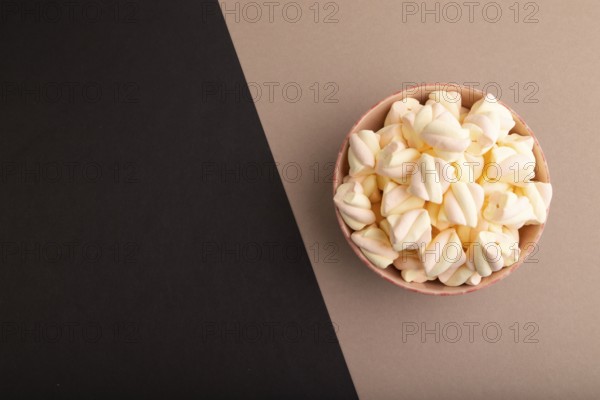 Orange and pink marshmallow in ceramic bowl on black and beige pastel paper background, top view, flat lay, copy space, minimalism
