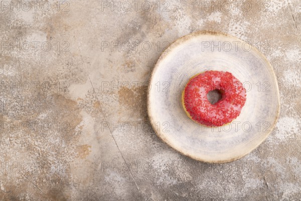 Pink Donut with sprinkles on blue ceramic plate on brown concrete background, top view, flat lay, copy space, minimalism