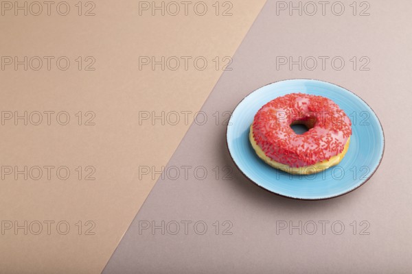 Pink Donut with sprinkles on blue ceramic plate on beige and gray pastel paper background, side view, copy space, minimalism
