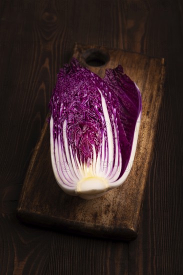 Purple Chinese cabbage on cutting board on brown wooden background, side view, close up, minimalism