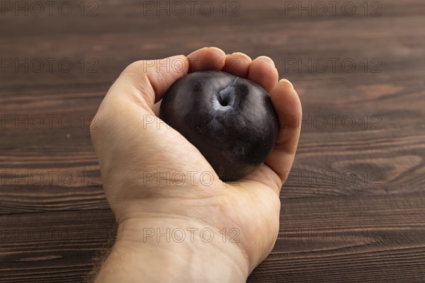 Purple Plum with hand on brown wooden background. Side view, close up. healthy food, vegetable, minimalism