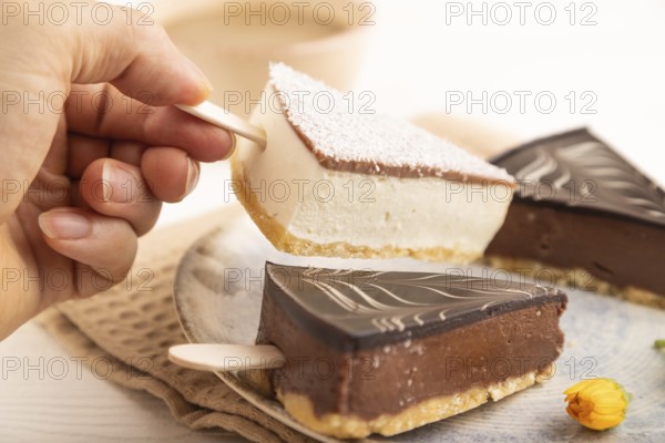 Chocolate and Vanilla Cake pops Marshmallow with hand with cup of coffee on white wooden background and beige linen textile. side view, close up, selective focus hold