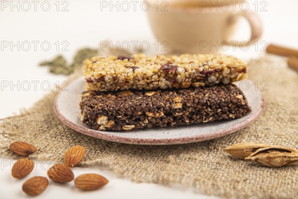 Granola bars with caramel, nuts, flakes in ceramic plate on white wooden background, beige linen napkin, cup of green tea. Side view, close up, selective focus
