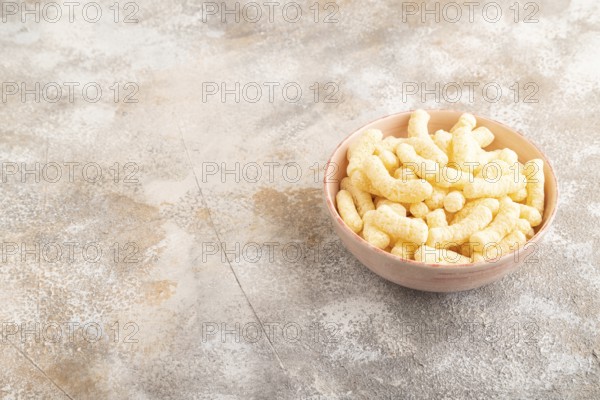 Corn flakes sticks with caramel in ceramic bowl on gray concrete background. Side view, copy space