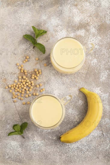 Organic non dairy banana and soy milk in glass on brown concrete background. Vegan healthy food concept, flat lay, top view, close up