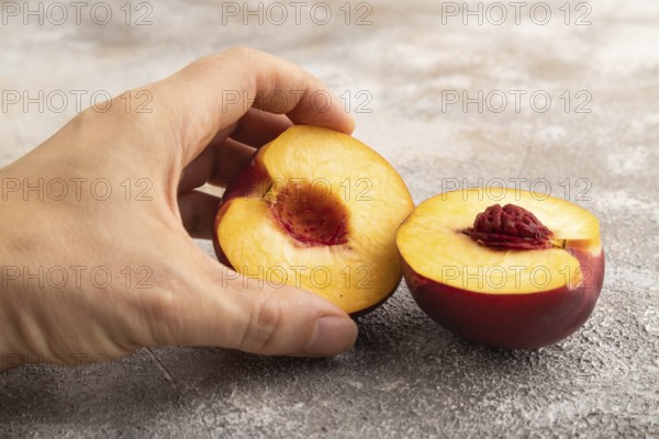 Peach Cut in half with hand on brown concrete background. Side view, copy space. healthy food, vegetable, minimalism