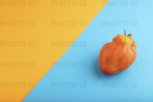 Red Heart Shape tomato on blue and orange pastel paper background. Side view, copy space. healthy food, vegetable, minimalism