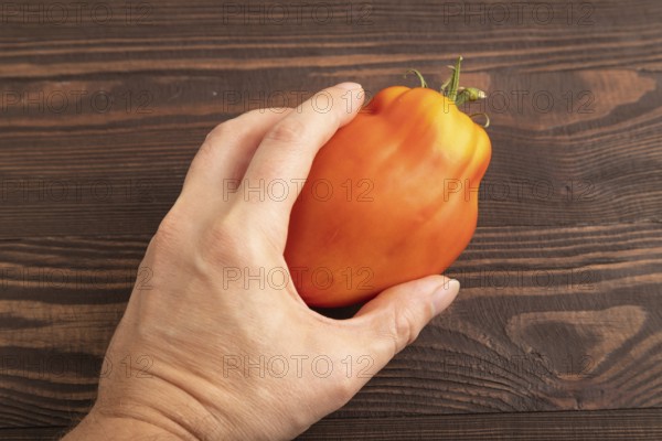 Red Heart Shape tomato with hand on brown wooden background. Top view, flat lay, close up. healthy food, vegetable, minimalism