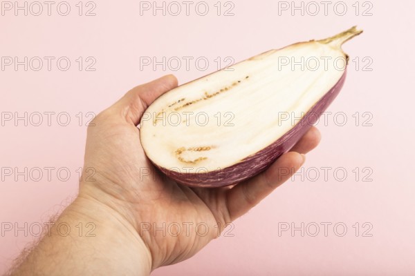 Hand holding sliced Purple eggplant with white stripes on pink pastel background. Side view, copy space. Tropical, healthy food, vegetable, minimalism