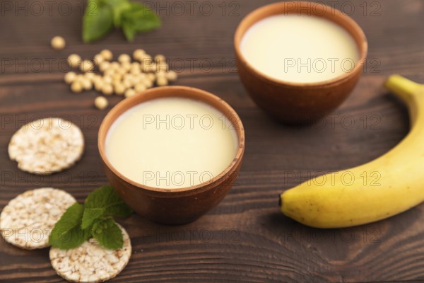 Organic non dairy banana and soy milk in clay cup on brown wooden background. Vegan healthy food concept, side view, close up, selective focus