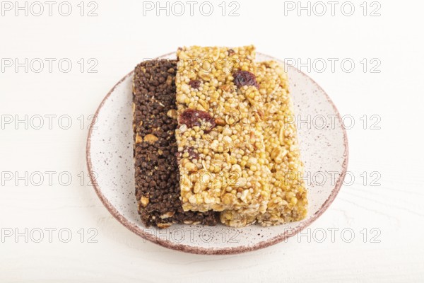 Granola bars with caramel, nuts, flakes in ceramic plate on white wooden background. Side view, close up