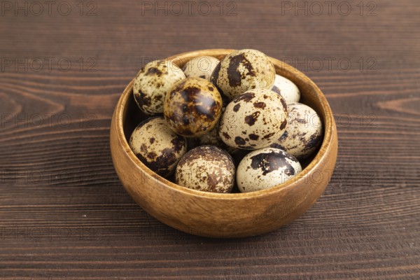 Pile of raw Quail eggs in bowl on a brown wooden background. side view, close up