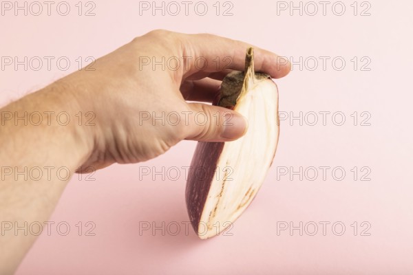 Hand holding sliced Purple eggplant with white stripes on pink pastel background. Side view, copy space. Tropical, healthy food, vegetable, minimalism