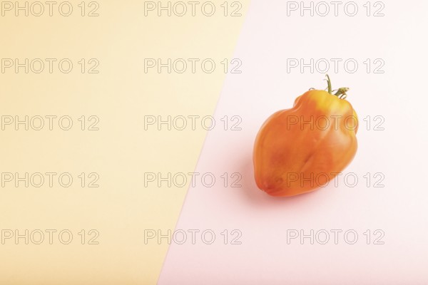 Red Heart Shape tomato on pink and orange pastel paper background. Side view, copy space. healthy food, vegetable, minimalism