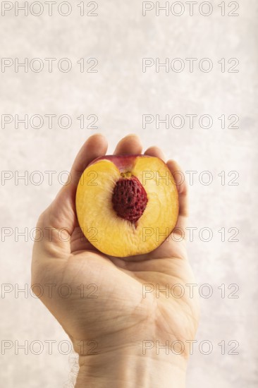 Peach Cut in half with hand on brown concrete background. Side view, copy space. healthy food, vegetable, minimalism