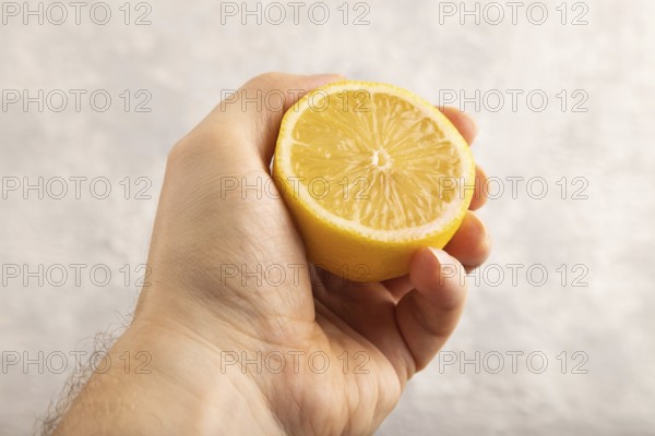 Yellow Lemon Cut in half with hand on gray concrete background. Side view, close up. healthy food, vegetable, minimalism. citrus