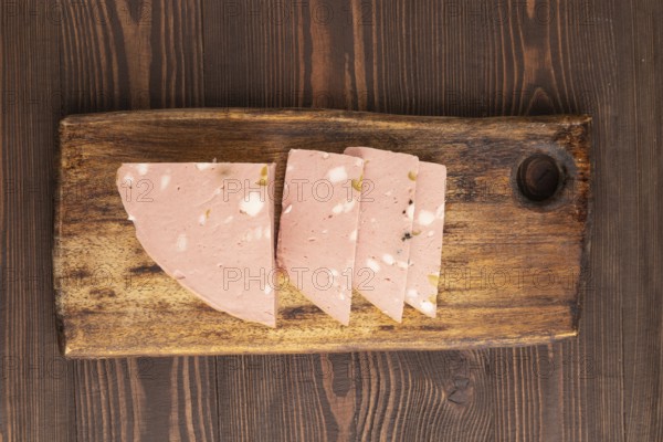 Mortadella sausage on wooden cutting board with pepper and herbs on brown wooden background. Top view, flat lay, close up