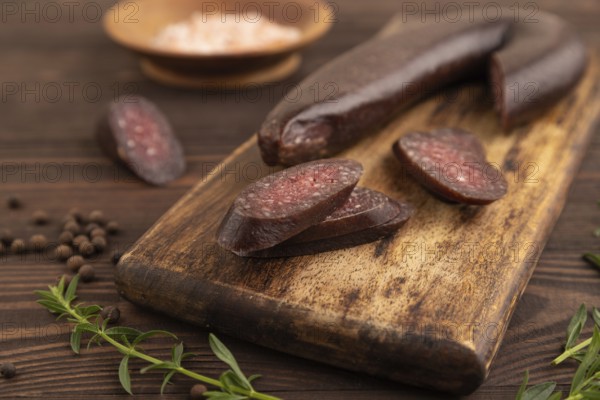 Sujuk sausage on wooden cutting board with pepper and herbs on brown wooden background. Side view, close up, selective focus