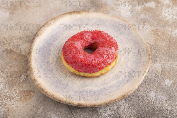 Pink Donut with sprinkles on blue ceramic plate on brown concrete background, side view, close up, minimalism