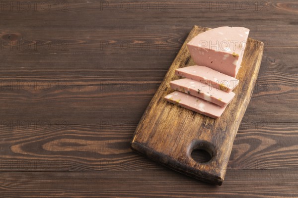 Mortadella sausage on wooden cutting board with pepper and herbs on brown wooden background. Side view, copy space