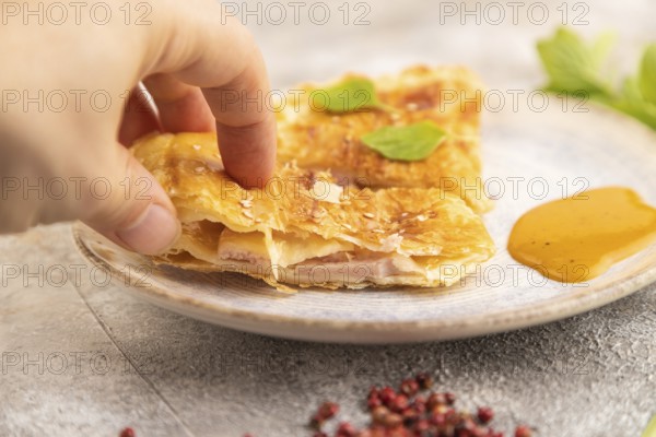 Fried homemade Khachapuri cake with hand with cheese and meat, fried in pan. Traditional Georgian cuisine on brown concrete background. Side view, close up, selective focus