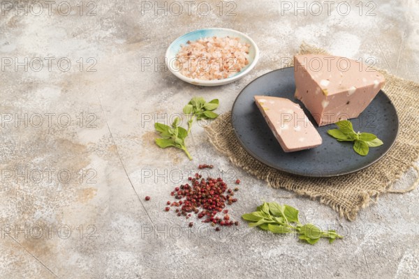 Mortadella sausage on plate with pepper and herbs on brown concrete background and linen textile. Side view, copy space