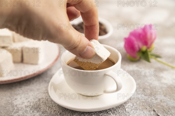 Coffee marshmallow with cup of coffee with hand on brown concrete background. side view, close up, selective focus