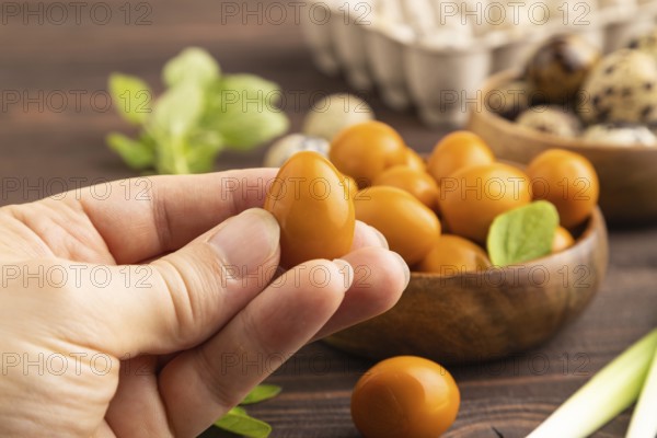 Pile of Smoked Quail eggs in bowl with hand on a brown wooden background. side view, close up, selective focus