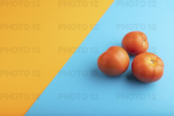 Red tomato on blue and orange pastel paper background. Side view, copy space. healthy food, vegetable, minimalism