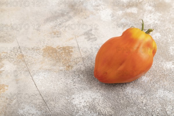 Red Heart Shape tomato on brown concrete background. Side view, copy space. healthy food, vegetable, minimalism