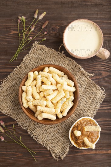 Corn flakes sticks with caramel in wooden bowl on brown wooden background and linen textile. Top view, flat lay, close up