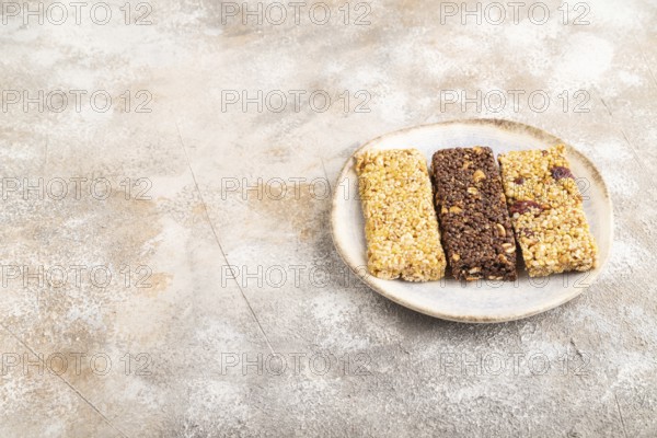 Granola bars with caramel, nuts, flakes in ceramic plate on brown concrete background. Side view, copy space