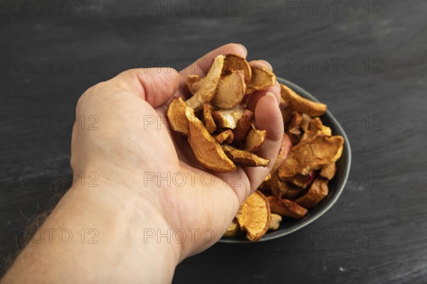 Dried Apples in ceramic bowl with hand on black wooden background. Side view, close up. healthy food, minimalism. sweet hold