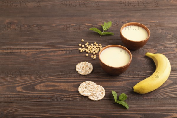Organic non dairy banana and soy milk in clay cup on brown wooden background. Vegan healthy food concept, flat lay, side view, copy space
