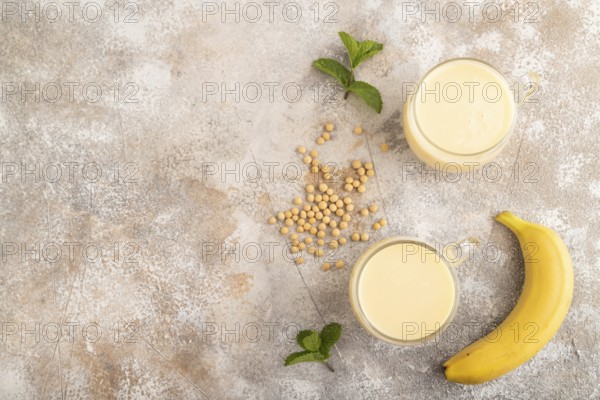 Organic non dairy banana and soy milk in glass on brown concrete background. Vegan healthy food concept, flat lay, top view, copy space
