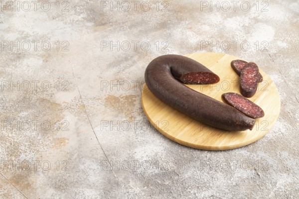 Sujuk sausage on wooden cutting board with pepper and herbs on brown concrete background. Side view, copy space