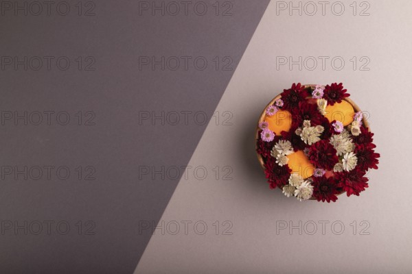 Wooden bowl with carrot slices and red Chrysanthemum flowers, Astrantia flowers, flower salad on beige and gray pastel paper background, top view, flat lay, copy space, minimalism