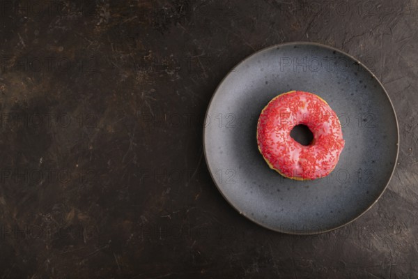 Pink Donut with sprinkles on blue ceramic plate on black concrete background, top view, flat lay, copy space, minimalism