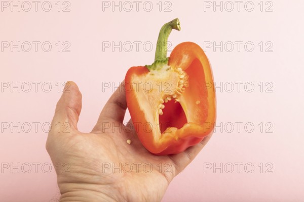 Hand holding sliced Red Cutted pepper on pink pastel background. Side view, copy space. Tropical, healthy food, vegetable, minimalism
