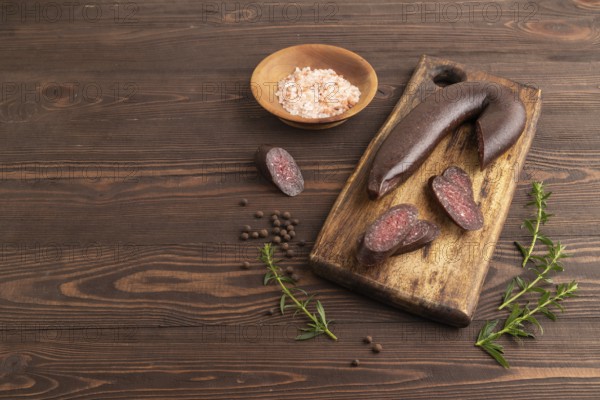 Sujuk sausage on wooden cutting board with pepper and herbs on brown wooden background. Side view, copy space
