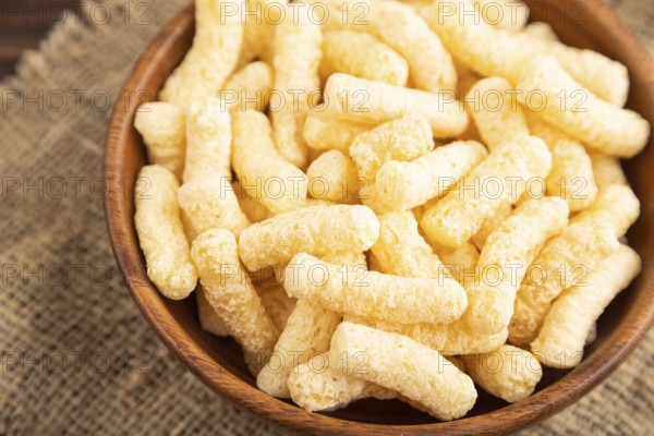Corn flakes sticks with caramel in wooden bowl on brown wooden background and linen textile. Side view, close up, selective focus