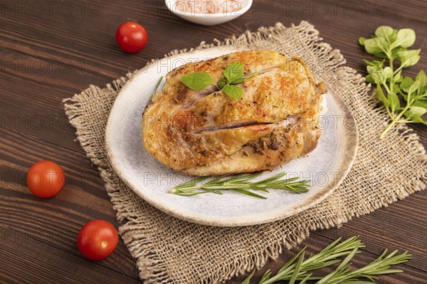 Fried Turkey Thigh with spices and rosemary on plate on brown wooden background and linen textile. side view, close up
